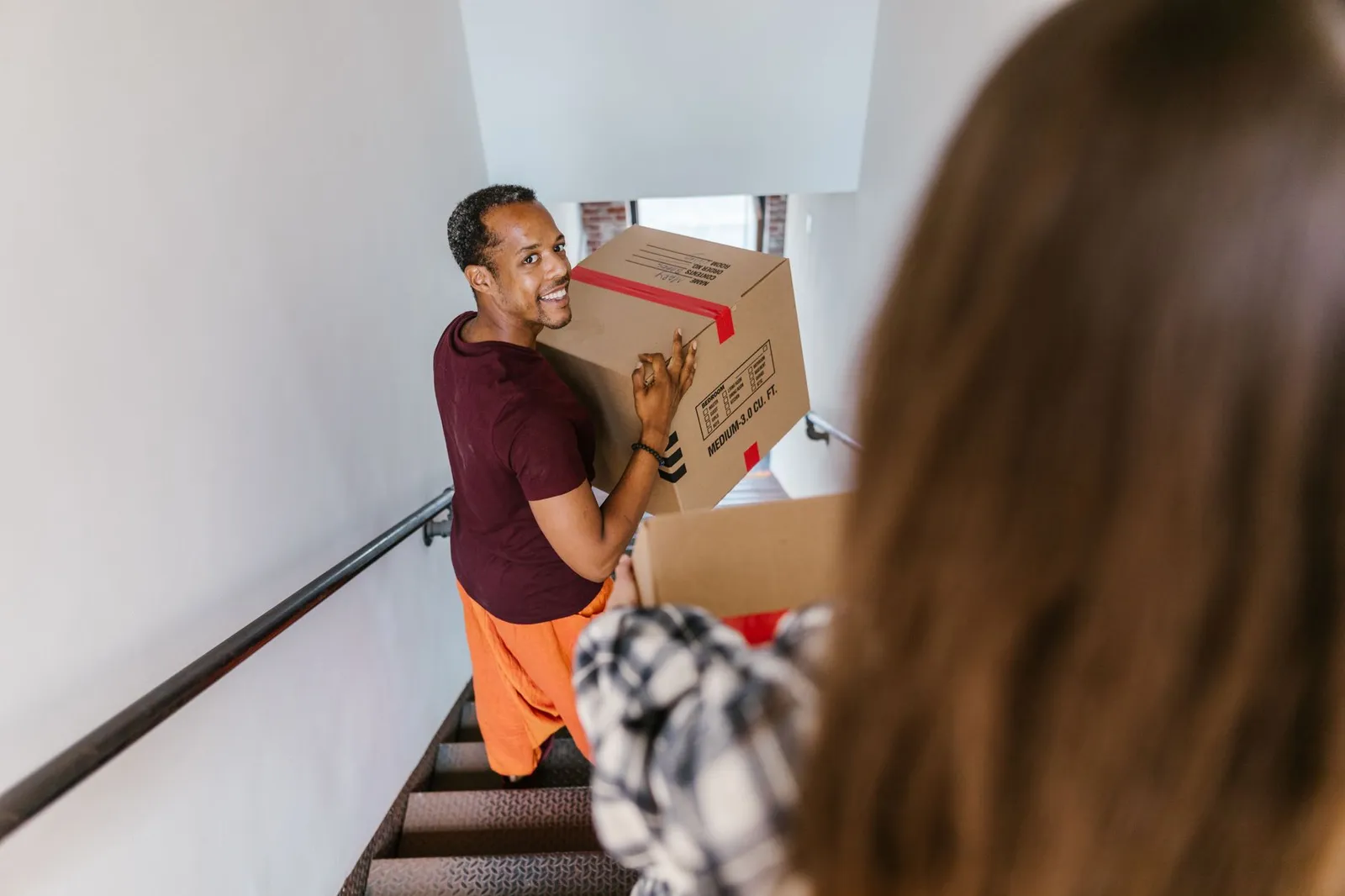 Mover carrying a box down an apartment stairwell for no-elevator junk removal in Gainesville